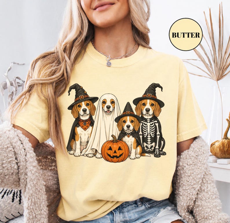 A woman wearing a yellow t-shirt with a graphic design of four dogs dressed in Halloween costumes, including a skeleton, a ghost, and a pumpkin.