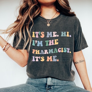 May include: A dark gray t-shirt with the text "It's me. Hi. I'm the pharmacist. It's me." printed in rainbow colors.