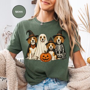 A woman wearing a green t-shirt with a Halloween-themed graphic of three dogs dressed in costumes, including a ghost and a skeleton.