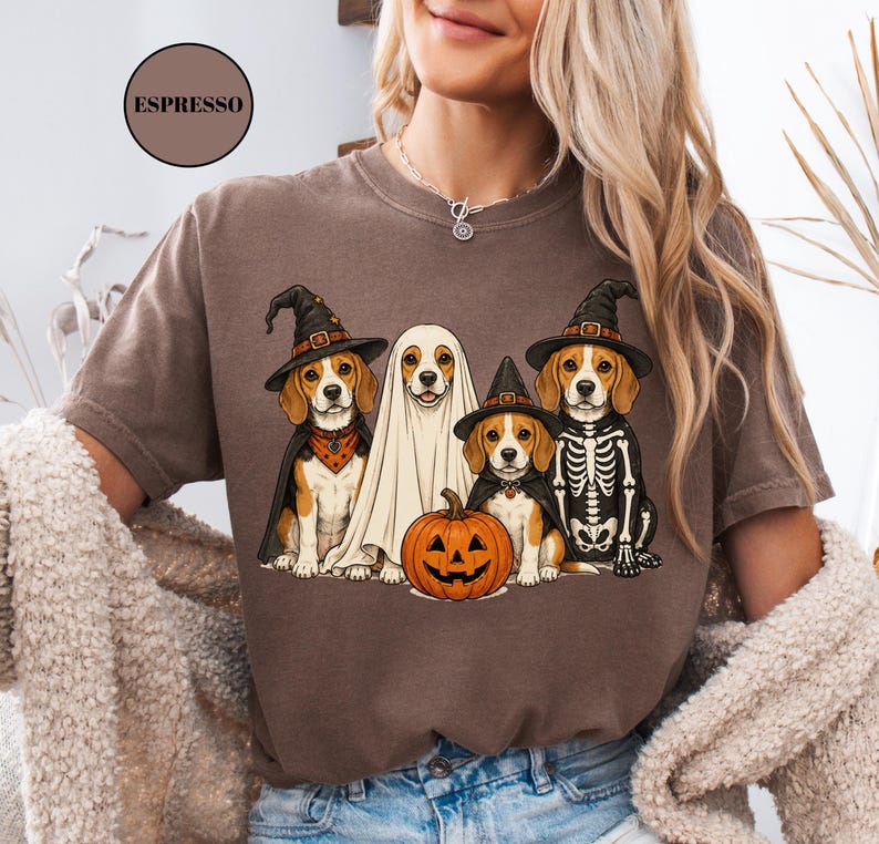 A woman wearing a t-shirt with a graphic design of four dogs dressed in Halloween costumes, including a ghost, skeleton, witch's hat, and pumpkin.