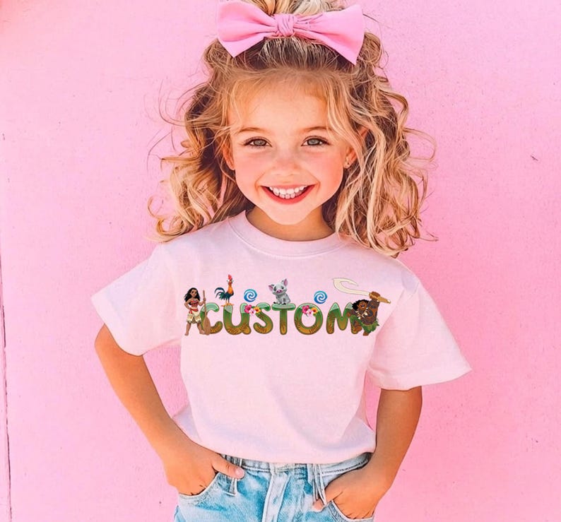 A young girl with curly blonde hair is smiling and wearing a pink bow in her hair. She is wearing a white t-shirt with the word "CUSTOM" printed on it.