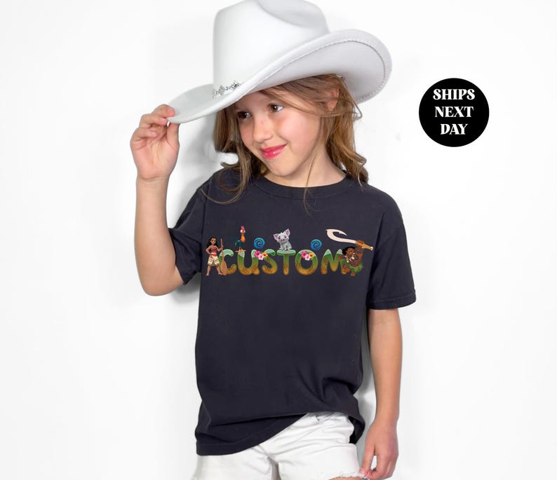 A young girl wearing a white cowboy hat and a black t-shirt with colorful text on it, posing for a photo.