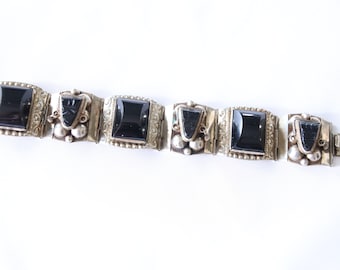May include: A silver bracelet with black onyx stones. The bracelet has a decorative design and a clasp.