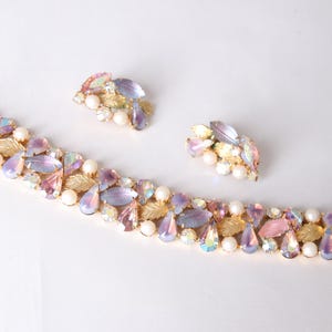 Könnte beinhalten: Ein Vintage-Schmuckset mit einem Armband und passenden Ohrringen. Das Armband und die Ohrringe sind mit schillernden, tropfenförmigen Kristallen, Kunstperlen und goldfarbenen Blattakzenten verziert. Das Set hat eine zarte, feminine Ästhetik.