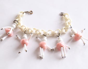 May include: A white plastic chain bracelet with pink and white beaded figures hanging from it. The figures are shaped like people with arms and legs.