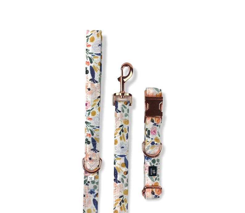 May include: A white dog collar and leash set with a floral pattern in shades of blue, pink, yellow, and green. The hardware is rose gold.
