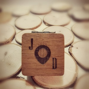 Può includere: Una scatola di legno con un coperchio incernierato, che presenta un design inciso a laser di una carta da gioco con la lettera 'J' e una nota musicale. La scatola è circondata da cerchi di legno.