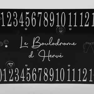 Peut inclure: Panneau rectangulaire noir avec des chiffres, du texte et des graphiques blancs. Le texte indique "Le Boulodrome d'Hervé". Les chiffres 0-13 sont affichés en haut et en bas. Comprend des smileys, des boules de pétanque et des chopes de bière.