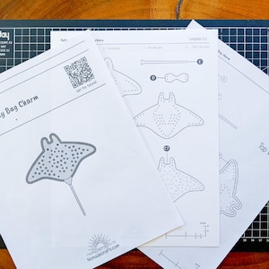 May include: White paper templates for a bag charm, with a stingray design and dotted patterns. The templates include diagrams, measurements in centimetres, and the website Nomadecrafts.com.
