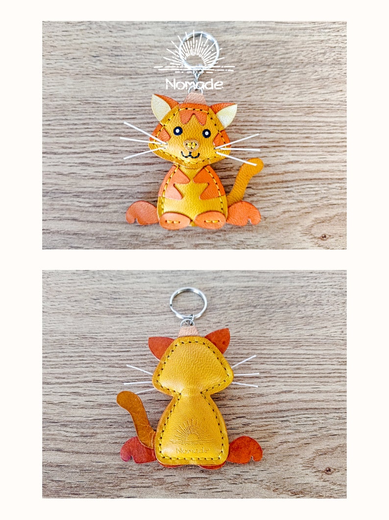 May include: A yellow leather cat keyring with orange accents. The cat is sitting with its tail curled around its legs. The keyring has a silver ring and the word "Nomade" is stitched on the back.