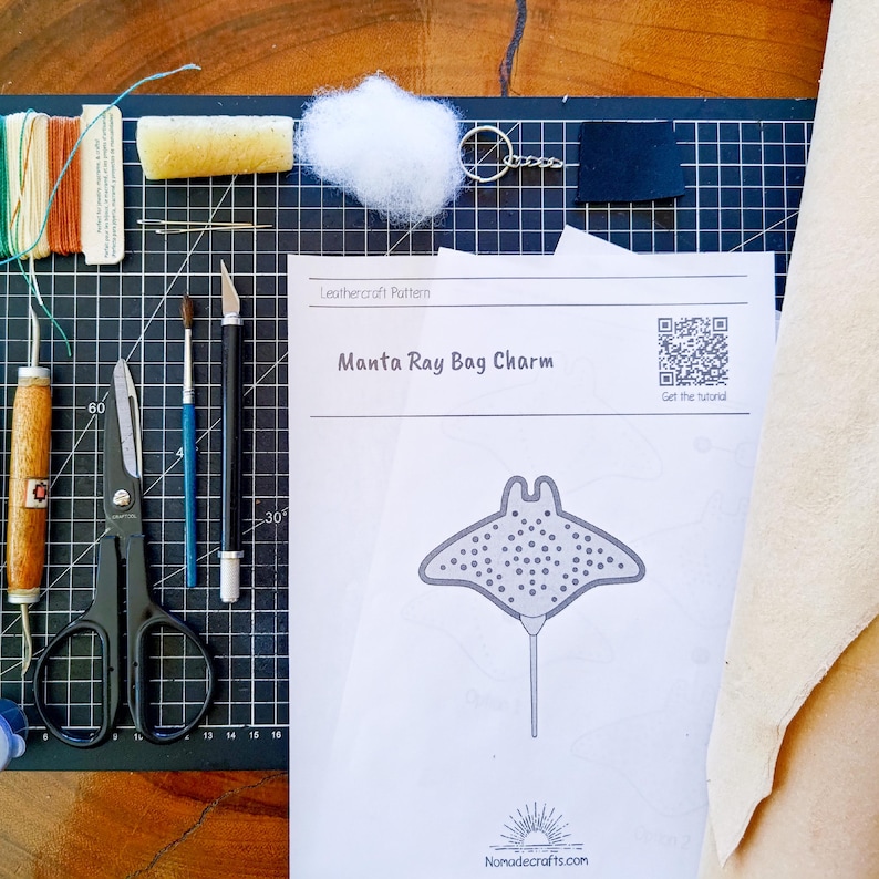 May include: A craft kit for a Manta Ray Bag Charm, with a printed pattern, tools, thread, and leather pieces. The kit includes scissors, a craft knife, brushes, and a key ring. The pattern shows a manta ray design with the text "Manta Ray Bag Charm".