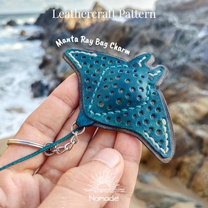 Puede incluir: Un charm de bolso de cuero turquesa con forma de manta raya, con un diseño perforado y costuras blancas. Está unido a un llavero y una cadena plateados. El texto "Leathercraft Pattern" y "Manta Ray Bag Charm" son visibles.
