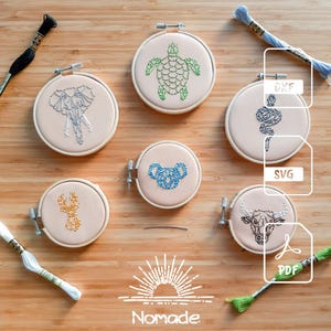 Puede incluir: Seis bastidores de bordado circulares de madera con tela que presenta diseños de animales bordados: tortuga, elefante, serpiente, koala, ciervo y toro. Incluye cuatro madejas de hilo en negro, azul, blanco y verde, y texto DXF, SVG y PDF.