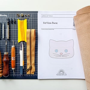 May include: A leathercraft pattern for a cat coin purse, with a template, tools, and a piece of leather. The tools include a leather punch, awl, stitching tools, a ruler, a cutting mat, and a zipper.