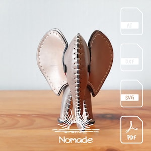 Peut inclure: Une figurine d'éléphant en cuir marron clair avec des détails cousus. La figurine est posée sur une surface en bois avec le mot "Nomade" imprimé en dessous. L'image comprend également des icônes pour les formats de fichiers AI, DXF, SVG et PDF.