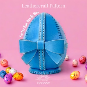 Peut inclure: Une boîte à bonbons en forme d'œuf en cuir bleu avec un nœud, des coutures blanches et le texte "Easter Egg Candy Box" et "Leathercraft Pattern". La boîte est sur un fond rose avec des bonbons colorés en forme d'œufs de Pâques.