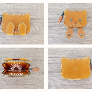May include: Four different views of a brown leather wallet with a cat design. The wallet has a zip closure and a small pocket on the front. The wallet is open in one view, showing a white sun design with the word "Nomade" printed on the inside.