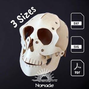 Puede incluir: Una máscara de calavera color crema construida con material en relieve superpuesto y remaches metálicos. El texto 3 Sizes es visible, junto con iconos de archivo etiquetados DXF, SVG y PDF. Un logo con el texto Nomade está abajo.