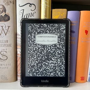 May include: A black and grey Kindle e-reader with a composition notebook screen saver that says "COMPOSITION KINDLE private thoughts" on a bookshelf with other books.