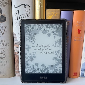 Könnte beinhalten: Ein schwarz-weißer Kindle E-Reader mit einem floralen Design und dem Text "so I will go to secret gardens in my mind". Der Kindle steht auf einem Regal mit einer Auswahl an Büchern.