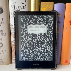 May include: A black and white Kindle e-reader with a composition notebook cover. The screen displays the text "COMPOSITION KINDLE" and "Allison Bailey".