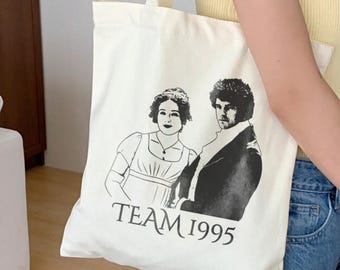 May include: White canvas tote bag with a black and white illustration of two people and the text "TEAM 1995".