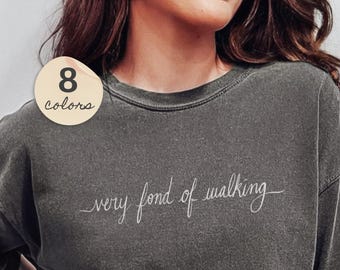 May include: A dark gray t-shirt with the text "very fond of walking" in white script. The shirt is available in 8 colors.