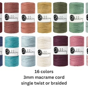 May include: Sixteen spools of 3mm macrame cord in various colors, single twist or braided. The spools are labeled "Bobbiny" and are arranged in rows. Colors include shades of red, brown, green, blue, and pink. The text "16 colors, 3mm macrame cord, single twist or braided" is below.