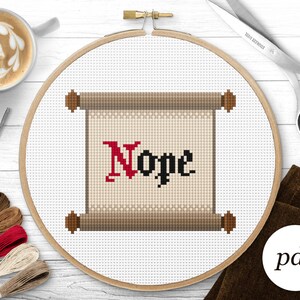 Op de afbeelding: Een kruissteekpatroon van een rol met het woord "Nope" in rode en zwarte letters. De rol is op een witte achtergrond en wordt omringd door een houten borduurring.