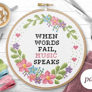 Op de afbeelding: Een witte borduurring met een bloemenontwerp en de tekst "Wanneer woorden falen, spreekt muziek".