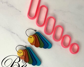 以下が含まれることがあります： ピンクの楕円形のクッキーカッター6個セットと、カラフルな粘土で作ったイヤリング2ペア。イヤリングは扇形になっていて、黄色、オレンジ、茶色、緑、青など様々な色が使われています。