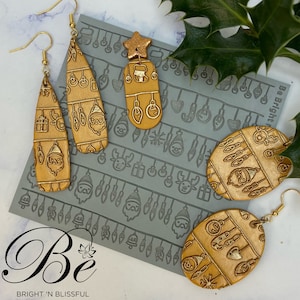 May include: Gold Christmas earrings with a festive design. The earrings are shaped like a teardrop and an oval. The design features a Santa Claus, a Christmas tree, and a gift. The earrings are on a gray background with a pattern of Christmas lights and ornaments.