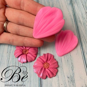Può includere: Stampi in silicone rosa per realizzare fiori in pasta polimerica. Gli stampi hanno la forma di petali di fiori e sono mostrati con due fiori in pasta polimerica finiti.