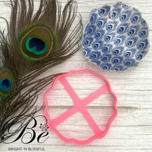 Può includere: Tagliapasta in plastica rosa a forma di fiore con quattro sezioni. Il tagliapasta è su una superficie di legno bianco.