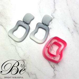 May include: A pair of grey ombre earrings with a silver accent and a pink plastic mould for making earrings.