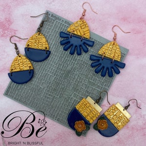 May include: Three pairs of handmade polymer clay earrings in a geometric design. The earrings feature a combination of gold and blue colors. The earrings are displayed on a gray textured surface with the text "Be Bright 'n Blissful".
