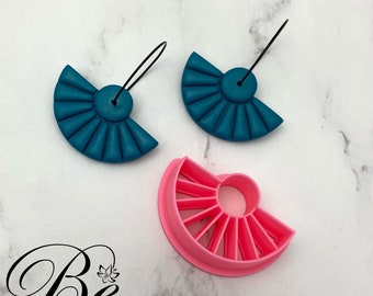 May include: A pair of teal blue fan-shaped earrings with black wire hooks. A pink plastic mold for making the earrings is also shown.