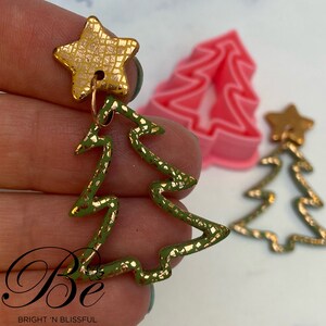 Può includere: Orecchini a forma di albero di Natale verde e dorati con un ciondolo a stella dorata. Gli orecchini sono realizzati in pasta polimerica e hanno una finitura testurizzata.