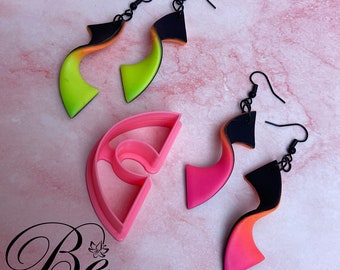 May include: Three pairs of colorful polymer clay earrings with black metal hooks. The earrings are shaped like a curved line with a gradient of color. The earrings are displayed on a pink surface with a pink plastic mold.