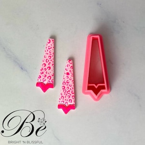 Puede incluir: Dos cortadores de fondant de estampado de leopardo rosa y blanco con un cortador rosa en forma de rectángulo alto.