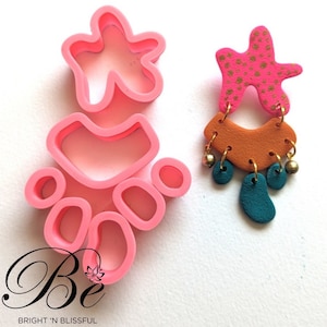 May include: Pink silicone moulds for making polymer clay earrings. The moulds are shaped like abstract shapes, including a star, a crescent moon, and several circles. The image also shows a pair of earrings made with the moulds, featuring pink, orange, and teal colours.