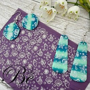 May include: A pair of teal and white seashell earrings with silver hooks. The earrings are on a purple background with a white seashell pattern. The text "Be Bright 'n Blissful" is at the bottom of the image.