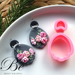 May include: A pair of grey polymer clay earrings with pink flower accents and silver earring hooks. A pink silicone mould for making the earrings is also shown.