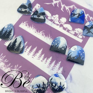 May include: A set of eight nail art stencils featuring different wintery scenes, including trees, mountains, and a moon. The stencils are made of a clear, flexible material and are reusable.