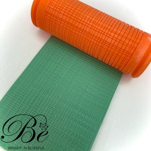 Peut inclure: Gros plan d'un rouleau à pâtisserie orange avec un motif en grille. Le rouleau à pâtisserie roule sur une feuille de fondant verte avec le même motif en grille. Le texte "Be Bright 'n Blissful" est visible dans le coin inférieur gauche de l'image.