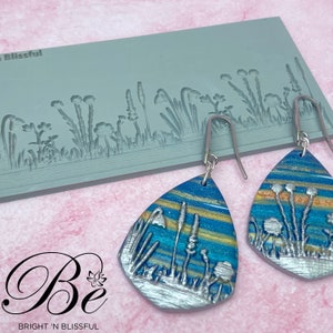 May include: A pair of silver teardrop-shaped earrings with a blue, yellow, and silver floral design. The earrings are made with polymer clay and have a textured surface. The earrings are shown next to a silicone mold with a floral design.