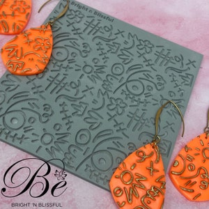 May include: A set of two orange teardrop-shaped earrings with gold accents. The earrings are made with a polymer clay mold featuring a pattern of abstract shapes and lines. The earrings are hanging from gold hooks. The mold is also shown in the image, with the text "Be Bright 'n Blissful".