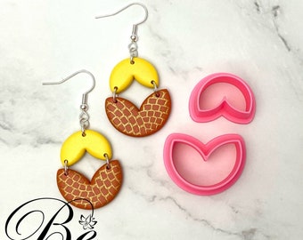 Peut inclure: Une paire de boucles d'oreilles pendantes jaunes et brunes avec un motif texturé. Les boucles d'oreilles sont en pâte polymère et sont accompagnées d'un jeu de découpoirs en pâte polymère rose.
