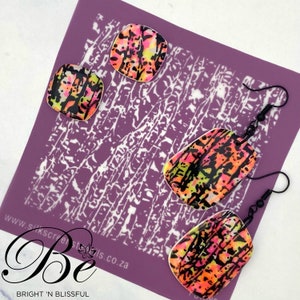 Könnte beinhalten: Ein Set aus vier Polymer Clay Ohrringen in einem abstrakten Muster in Schwarz, Pink, Gelb und Orange. Die Ohrringe werden auf einem violetten Hintergrund mit einer weißen Schablone präsentiert.