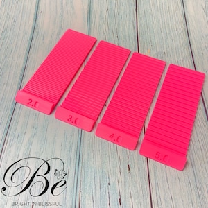 May include: Four pink plastic tile spacers, labelled 2.0, 3.0, 4.0, and 5.0. These spacers are used to create even gaps between tiles during installation.